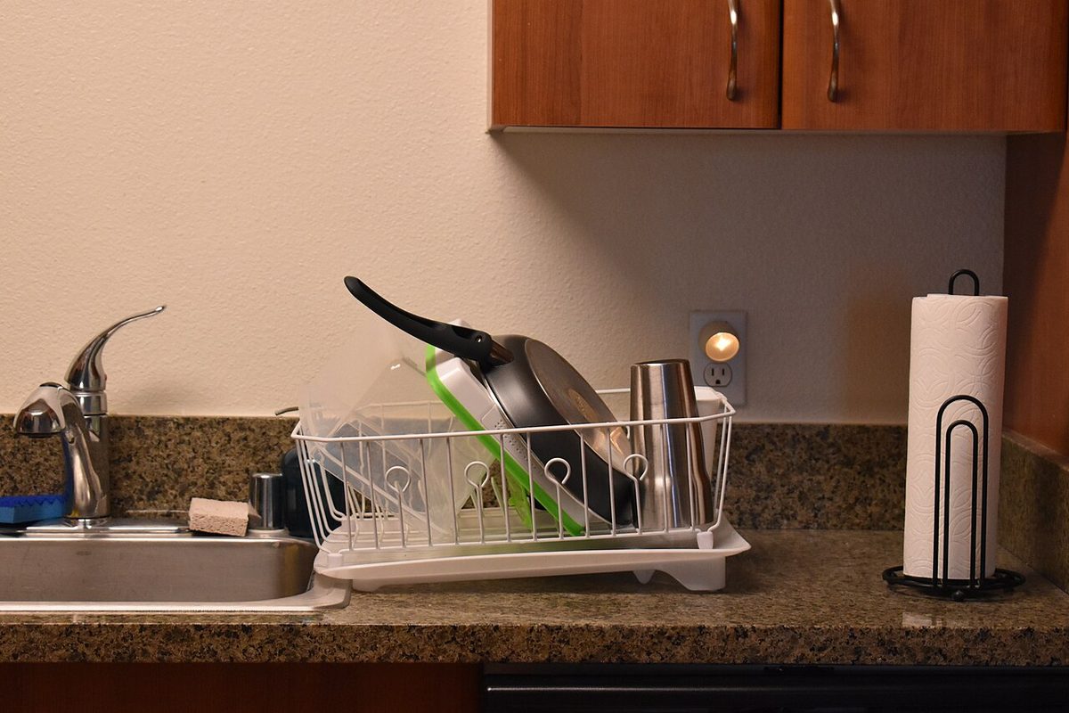 A dish drying rack beside a kitchen sink under wooden cabinets