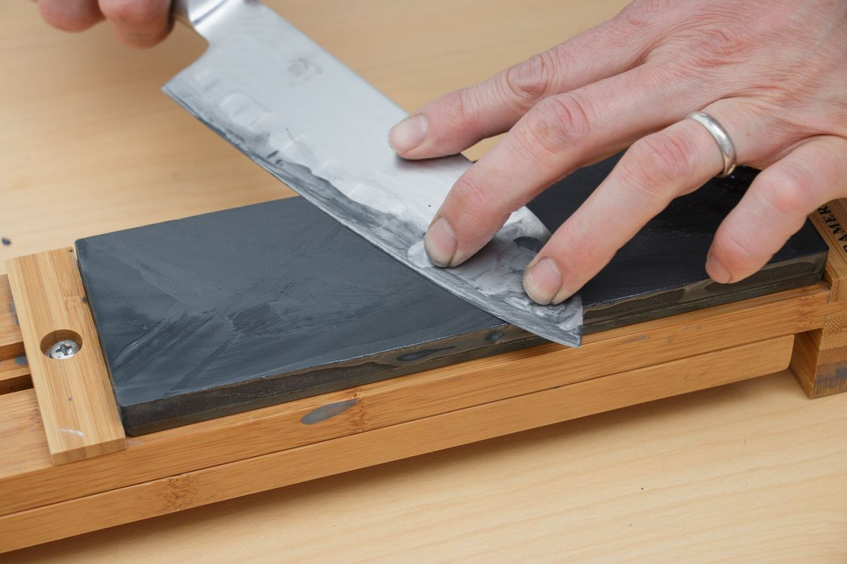 Hands drawing a kitchen knife across a sharpening whetstone