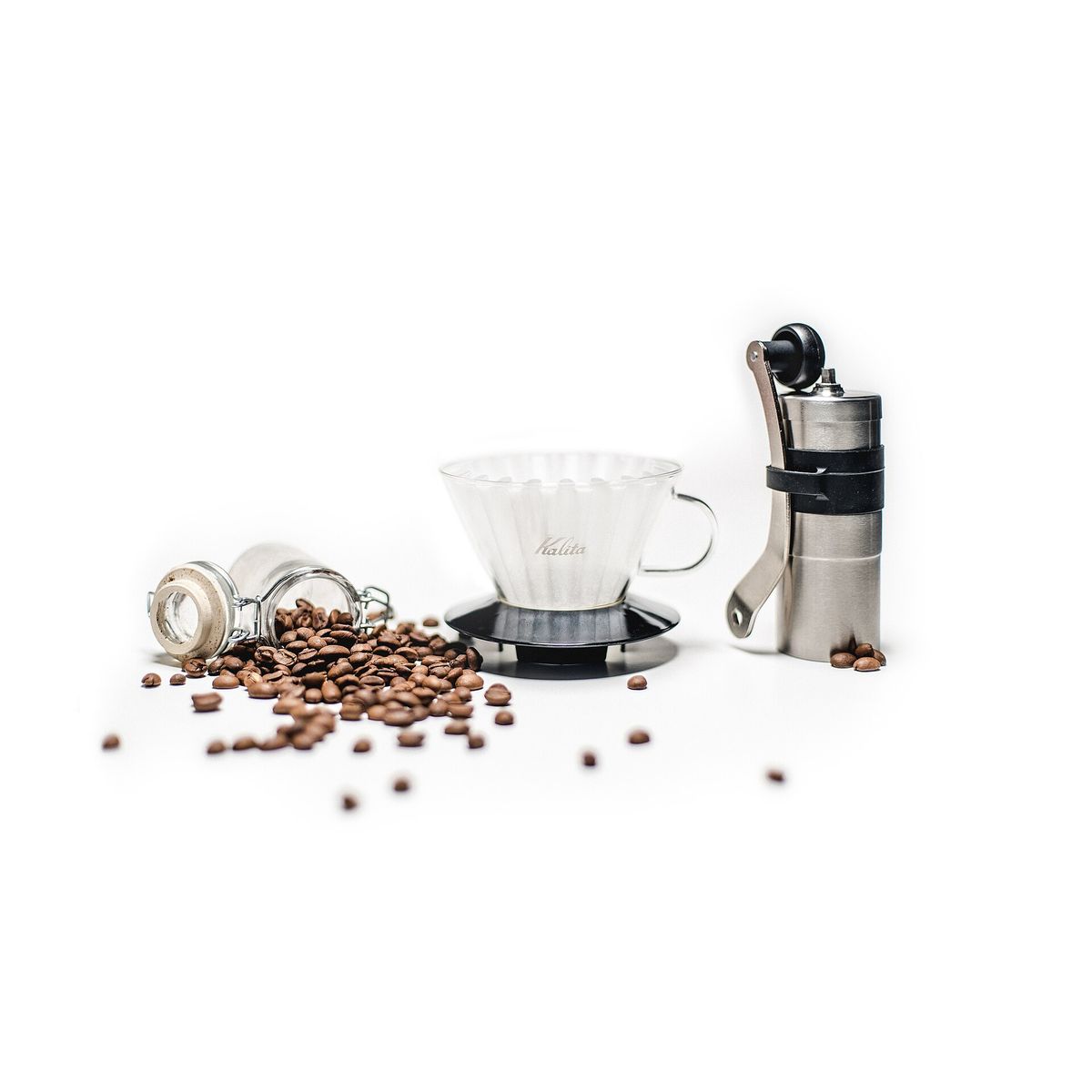 A glass pour-over dripper and a hand grinder beside scattered coffee beans